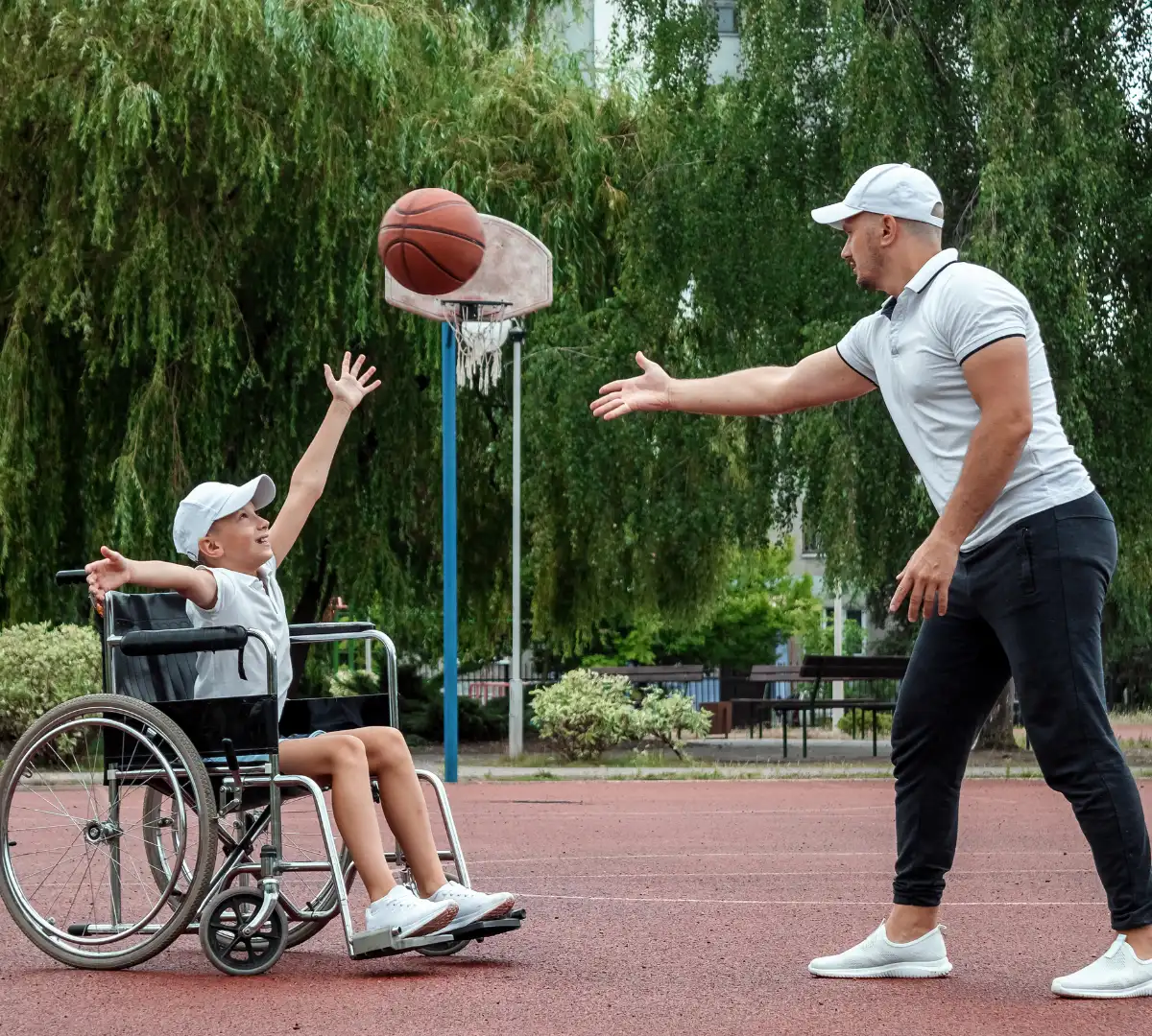 Disabled boy in wheelchair playing basketball with dad