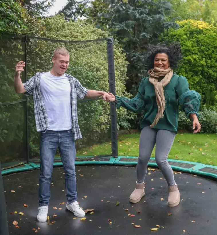 Disabled boy and support worker jumping on trampoline
